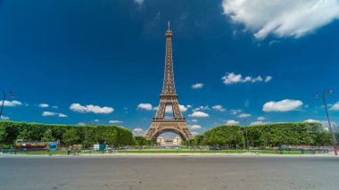 Paris 'teki Champs de Mars' taki Eyfel Kulesi. Zaman atlaması, Fransa. Yazın mavi bulutlu gökyüzü, yeşil çimenler ve etrafta trafik olan çeşme.