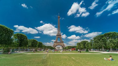 Paris 'teki Champs de Mars' taki Eyfel Kulesi. Zaman atlaması, Fransa. Yazın mavi bulutlu gökyüzü yeşil çimlerle kaplı ve insanlar etrafta dolaşıyor. İlerliyorum.