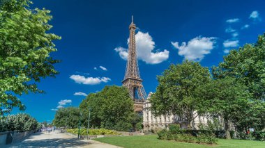 Eiffel Kulesi, Paris 'teki Siene nehri kıyılarından gösterildi. Zaman ayarlı hiperhız, Fransa. Yazın mavi bulutlu gökyüzü Yeşil ağaçlar ve etrafta yürüyen insanlar