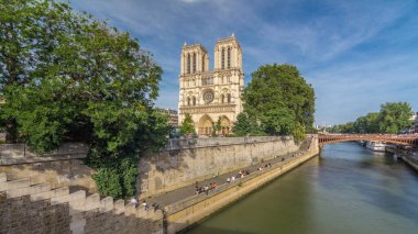 Notre Dame de Paris katedralinin ön cephesinde, nehir ve kıyı şeridi hiperhızlandırılmış. Köprüden panoramik görüntü. Yazın mavi bulutlu gökyüzü