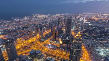 Dubai'de şehir merkezi ve finans bölgesi gece saati. Bulutlu gökyüzü ve karayolu üzerinde trafik. Burç Halife bakış açısından kuleler ve gökdelenler ile havadan görünüm.