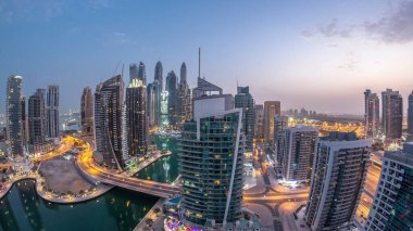 Dubai Marina konutları ve ofis gökdelenlerinin panoramik hava manzarası. Gün doğumundan önce gece gündüz geçiş zamanı. Yüzen tekneler ve yatlar. Yolda trafik vardı.