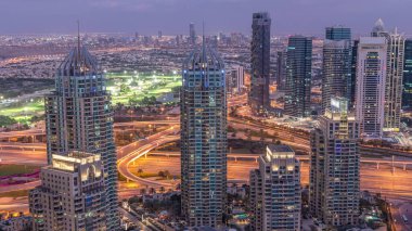 Dubai Marina gökdelenleri ve Jumeirah göl kuleleri Birleşik Arap Emirlikleri 'nde hava gününden geceye geçiş zamanlarını gösteriyor. Kavşağı olan bir yolda trafik