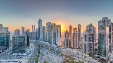 Günbatımında Business Bay, Dubai, Uae 'de bulunan birçok gökdelenle modern yerleşim ve ofis kompleksi. Körfez Bulvarı Parkı 'nın yanındaki büyük otoparkta arabalar ve trafik vardı.