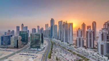 Günbatımında Business Bay, Dubai, Uae 'de bulunan birçok gökdelenle modern yerleşim ve ofis kompleksi. Körfez Bulvarı Parkı 'nın yanındaki büyük otoparkta arabalar ve trafik vardı.