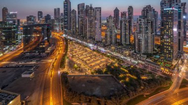 Business Bay, Dubai, Uae 'de birçok gökdelenden geceye geçiş süresine sahip konut ve ofis kompleksi. Körfez Bulvarı Parkı 'nın yanındaki büyük otoparkta arabalar ve trafik vardı.