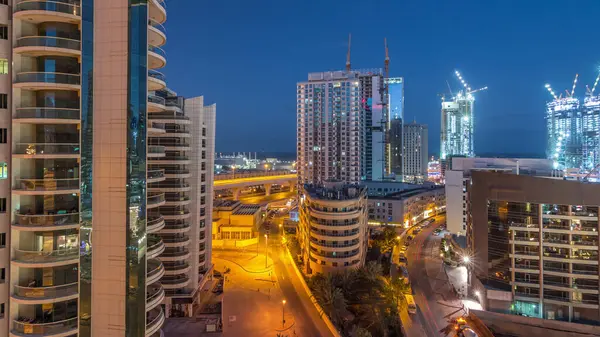 Dubai Marina 'da aydınlık gökdelenler ve gece gündüz gezinti güvertesi geçiş zamanı. Yol trafiği olan modern kuleler ve tekneler. Birleşik Arap Emirlikleri