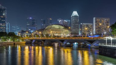 Aydınlatılmış Double Esplanade Tiyatrosu, Esplanade Drive 'ın arkasındaki trafik saatinde hız sınırını aştı. Singapur gökdelenleri arka planda gökdelenler