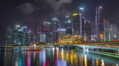 Esplanade Köprüsü ve şehir merkezindeki gökdelenler arka planda Singapur 'da gece vakti hızlandırılmış. Aydınlatılmış kuleler suya yansıyor