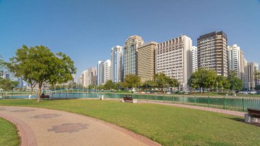 Abu Dabi 'nin sahil şeridi boyunca uzanan Corniche Bulvarı plajı parkında arka planda gökdelenler var. Lake Park 'ın manzarası. Bir tarafta ağaçlar. Güneşli bir günde mavi gökyüzü
