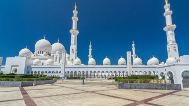 Birleşik Arap Emirlikleri 'nin başkenti Abu Dabi' deki Şeyh Zayed Büyük Camii zaman atlaması. Kubbeler ve minarelerle yan manzara. Ön planda çalılıklar. Güneşli bir günde mavi gökyüzü