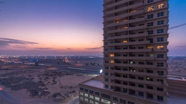 Ajman 'da çatıdan gece kuleye kule ve kavşakta trafik olan şehir manzarası. Birleşik Arap Emirlikleri 'nde gün batımından sonra aydınlanan binaların hava manzarası.