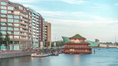Sudaki pagoda şeklinde bir Çin restoranının hipervanesi, tarihi şehir merkezi binalarının ve günbatımında modern mimarinin arka planına karşı kurulur. Amsterdam, Hollanda