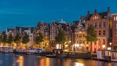 Amstel Nehri 'ndeki ünlü Dansçı Evleri' nin panoramik zaman atlaması gece gündüz geçişi. Tekneli su kanalları. Hollanda, Amsterdam 'da ikonik dönüm noktası