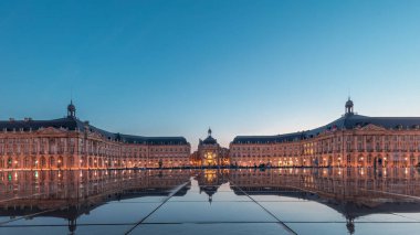 Place de la Bourse ve Miroir d 'eau Bordeaux, Fransa' daki panoramik zaman geçişi aydınlanmış mimariyi yansıtıyor. Tramvay ve tramvay geçen şehir ve çeşme.