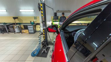 Araba tamircisi kırmızı arabayı asansörden tekerlere hizalama kamerasını tamir istasyonunda kontrol ediyor. Yan görünüm