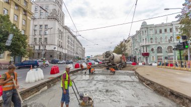 Turuncu üniformalı ve mikser makineli işçilerle yol inşaatı için somut çalışmalar ve sıkıştırma. Tramvay raylarının yeniden inşası