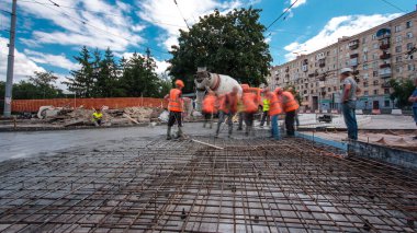 Tramvay rayları onarılan ve bakım süreleri yüksek olan yol inşaatı. Metal bir şebekeye beton dökülüyor. Kavşağın ortası. Arkaplanda yeşil ağaçlar