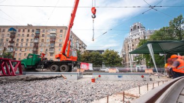 Turuncu vinçle kamyondan beton plakaları indirip yüklüyorlar. Tramvay rayları onarımı ve bakım süreleri olan yol inşaatı kavşağın orta kısmında hızlandırılmış..