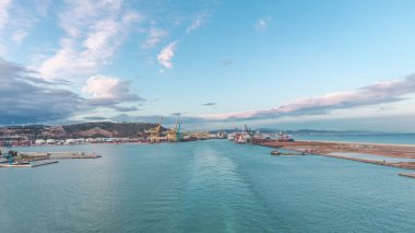 Gün batımında açık denizde yelken açan gemiden dalgalı ve limanlı deniz manzarası. Barselona kıyısı, İspanya