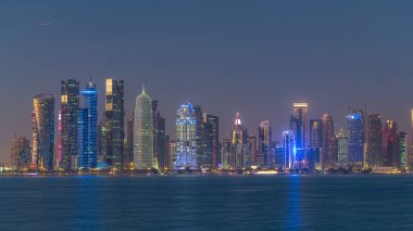 Doha şehir merkezi ufuk çizgisi günden geceye geçiş zamanı, Katar, Orta Doğu. Batı Körfezi 'ndeki aydınlık gökdelenler Körfez suyuna yansıyor.