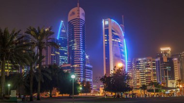 Doha 'nın yüksek katlı bölgesinde gece vardiyası, parktan görülmüş. Batı körfezinde aydınlatılmış gökdelenler ve palmiyeler