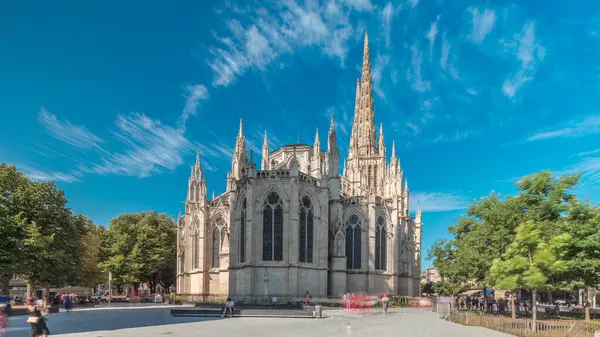 Saint-Andre de Bordeaux Katedrali. Mavi gökyüzünün altında ikiz kuleleri olan hızlandırılmış zaman atlaması. Yeşil ağaçlar ve meydanda yürüyen insanlar sakin bir şehir atmosferi yaratıyor. Bordeaux, Fransa