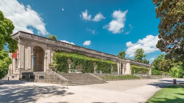 Fransa 'nın başkenti Jardin' de Palais du Capitole 'de zaman atlaması. Sarmaşık kaplı yeşil ağaçlar, merdivenler ve parlak mavi bulutlu gökyüzü ile çevrili tarihi bir binanın manzarası.