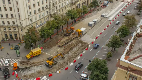 Turuncu inşaat teleskopik vinç eski tramvay raylarını kamyon saatine yüklüyor. Şapkalı ve üniformalı endüstriyel işçiler. Şehir caddesindeki tramvay raylarının yeniden inşası