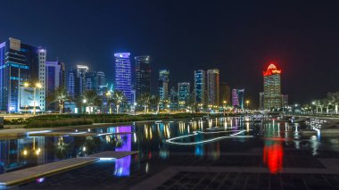 Geceleri Doha 'nın ufuk çizgisi. Yıldızlı gökyüzü Park Timelapse hiper hızından görünüyor, Katar. Aydınlatılmış gökdelenler ve kuleler çeşme suyuna yansıyor
