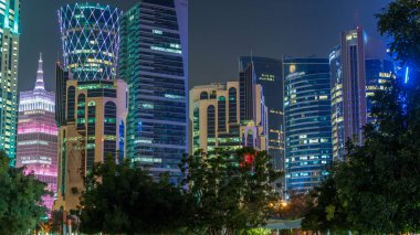 Geceleri Doha 'nın ufuk çizgisi. Yıldızlı gökyüzü Park Timelapse, Katar' dan görülüyor. Ön planda ağaçlar. Aydınlatılmış gökdelenler ve kuleler