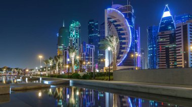 Geceleri Doha 'nın ufuk çizgisi. Yıldızlı gökyüzü Park Timelapse, Katar' dan görülüyor. Aydınlatılmış gökdelenler ve kuleler çeşme suyuna yansıyor