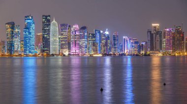 Doha şehir merkezi ufuk çizgisi günden geceye geçiş zamanı, Katar, Orta Doğu. Batı Körfezi 'ndeki aydınlık gökdelenler Körfez suyuna yansıyor. MIA parkından görüntü