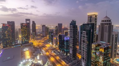 Batı Körfezi bölgesinin ufuk çizgisi Doha 'da günden geceye geçiş zamanı, Katar. Günbatımından sonra modern gökdelenlerin çatıdan görünüşü aydınlandı. Yolda trafik vardı.