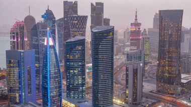 Batı Körfezi bölgesinin ufuk çizgisi Doha 'da günden geceye geçiş zamanı, Katar. Günbatımından sonra modern gökdelenlerin çatıdan görünüşü aydınlandı. Yolda trafik vardı.
