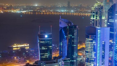 Katar 'ın Doha Zaman Çizelgesi' nde Batı Körfezi bölgesinin ufuk çizgisi. Aydınlatılmış modern gökdelenler geceleri çatıdan gökyüzü manzarası. Arka plandaki körfez ve yoldaki trafik