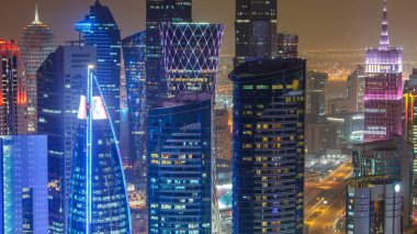 Katar 'ın Doha Zaman Çizelgesi' nde Batı Körfezi bölgesinin ufuk çizgisi. Aydınlatılmış modern gökdelenler geceleri çatıdan gökyüzü manzarası. Yolda trafik vardı.