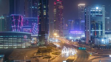 Katar 'ın Doha Zaman Çizelgesi' nde Batı Körfezi bölgesinin ufuk çizgisi. Aydınlatılmış modern gökdelenler geceleri çatıdan gökyüzü manzarası. Yolda trafik vardı.