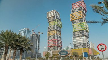 Renkli Al Marina İkiz Kuleleri binasıyla Doha ufuk çizgisi zaman çizgisi Katar 'ın başkenti Lusail' de yer almaktadır. Palmiyeler ve ağaçlar. Yolda trafik vardı.