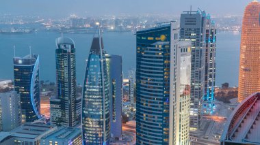 Batı Körfezi bölgesinin ufuk çizgisi, Doha 'da günden geceye geçiş, Katar. Günbatımından sonra modern gökdelenlerin çatıdan görünüşü aydınlandı. Yollarda trafik, arka planda körfez