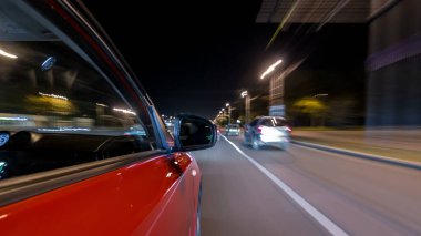 Hızlı arabanın yanından gelen bir drivelapse, gece caddesinde hızla ilerliyor. Işıklar yüksek hızda arabayı yansıtıyor. Modern bir şehrin hızlı ritmi. Bulanık hareket