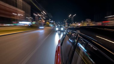 Hızlı arabanın yanından gelen bir drivelapse, gece caddesinde hızla ilerliyor. Işıklar yüksek hızda arabayı yansıtıyor. Modern bir şehrin hızlı ritmi. Bulanık hareket