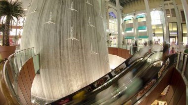 Şelalenin içinde yürüyen merdivende bir sürü insan var. Dünyanın en büyük alışveriş merkezi Dubai, Birleşik Arap Emirlikleri zaman çizelgesi.