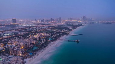Dubai 'deki Dubai marina gökdelenlerini ve BAE' deki plajları gece gündüz gösteren gökyüzü görüntüsü. Helikopter pistinden hava manzarası