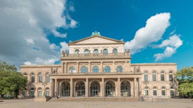 Hanover Devlet Operası 'nın (Staatsoper Hannover) ön görüntüsü. Şehir meydanında canlı mavi bulutlu bir zaman dilimi altında yürüyen insanların olduğu klasik tarzda bir tiyatro. Almanya