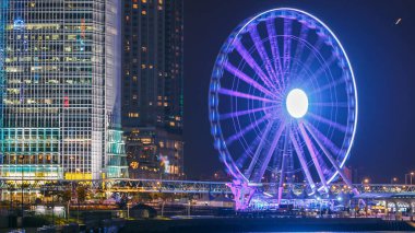 Gökdelenler gece zaman çizelgesi ve Hong Kong Gözlem Çarkı, şehirdeki en son turistik mekan. Rıhtımda yürüme alanı ve suda yansıma.