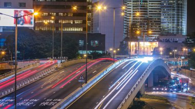 Geceleyin Hong Kong İş Bölgesi zaman çizelgesi. Arka taraftaki şirket binası ve yoğun trafiği köprünün yoğun olduğu saatte ana caddenin karşısındaki üst geçitte..