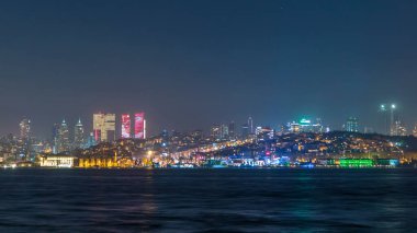 Night timelapse view of besiktas district with some illuminated skyscrapers in Istanbul taken from asian part of the city. Reflection on Bosphorus water