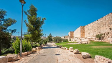 Antik kutsal Kudüs zaman tünelinin savunma duvarı. Parlak güneş tarafından aydınlatılan hiperhız. Yürüyüş yolu ve mavi gökyüzü yakınında harika yeşil çimenler.