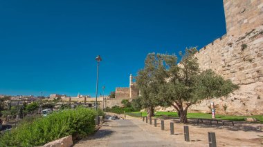 Antik kutsal Kudüs zaman tünelinin savunma duvarı. Parlak güneş tarafından aydınlatılan hiperhız. Harika yeşil çimenler ve mavi gökyüzü. Yolda trafik vardı.